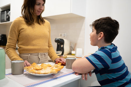 Mother and son enjoying a sweet treat and engaging in conversation in their bright, modern kitchenの写真素材