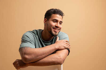 Portrait of a happy man sitting on chair with arms crossed, looking away and smiling on beige backgroundの写真素材