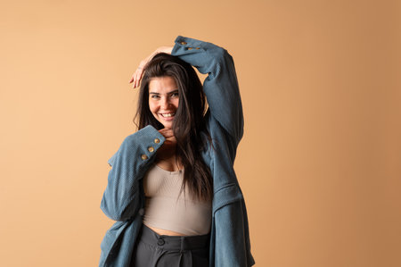 Studio portrait of a cheerful young latin woman touching her hair while smiling on a beige backgroundの写真素材
