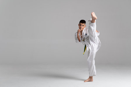 Young boy practicing kyokushinkai karate, kicking high with strength and focus in a bright studioの写真素材