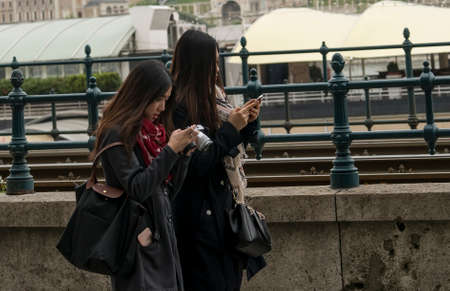 Budapest, Hungary - April 11,2016: Two young Chinese girl walking by the fence and play with mobile phone.のeditorial素材