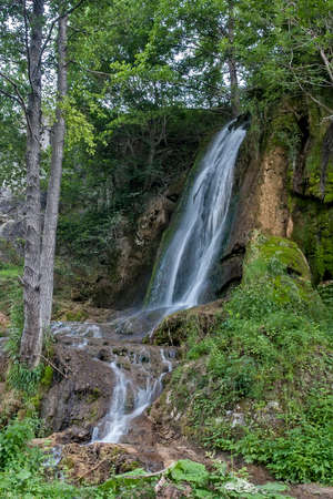 Waterfall on a mountain stream with rocks covered with mossの写真素材