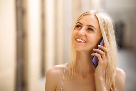 Photo of cute charming young lady wear white clothes walking talking modern gadget smiling outside urban city streetの写真素材