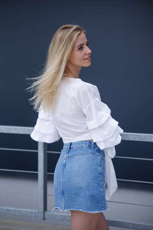 Beautiful blonde fashionable sexy tourist girl walking in city street. Woman looking at camera outdoors wearing trendy white t-shirt, denim jean short skirt.の写真素材