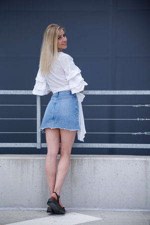 Beautiful blonde fashionable sexy tourist girl walking in city street. Woman looking at camera outdoors wearing trendy white t-shirt, denim jean short skirt.の写真素材
