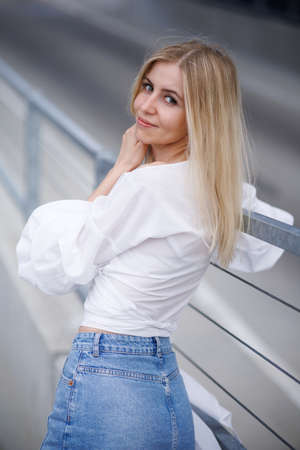 Beautiful blonde fashionable sexy tourist girl walking in city street. Woman looking at camera outdoors wearing trendy white t-shirt, denim jean short skirt.の写真素材