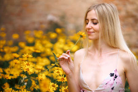 Fresh portrait pretty woman with sexy lips with make-up in pink dress with amazing yellow flowers. Gorgeous glamorous girl looks at flowers. beauty lady.の写真素材