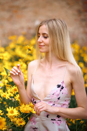 Fresh portrait pretty woman with sexy lips with make-up in pink dress with amazing yellow flowers. Gorgeous glamorous girl looks at flowers. beauty lady.の写真素材