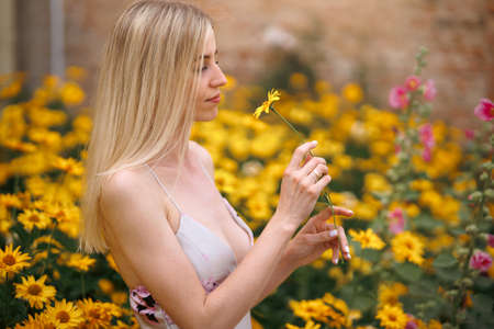 Fresh portrait pretty woman with sexy lips with make-up in pink dress with amazing yellow flowers. Gorgeous glamorous girl looks at flowers. beauty lady.の写真素材