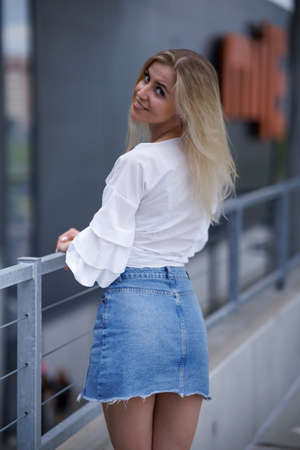 Beautiful blonde fashionable sexy tourist girl walking in city street. Woman looking at camera outdoors wearing trendy white t-shirt, denim jean short skirt.の写真素材