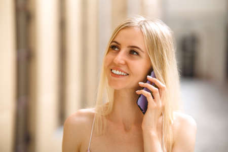 Photo of cute charming young lady wear white clothes walking talking modern gadget smiling outside urban city streetの写真素材