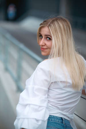 Beautiful blonde fashionable sexy tourist girl walking in city street. Woman looking at camera outdoors wearing trendy white t-shirt, denim jean short skirt.の写真素材