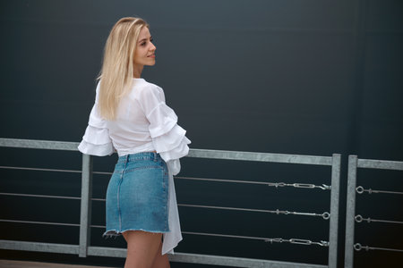 Beautiful blonde fashionable sexy tourist girl walking in city street. Woman looking at camera outdoors wearing trendy white t-shirt, denim jean short skirt.の写真素材