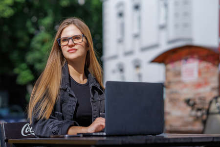 Professional young business woman in sexy glasses in black jeans jacket is working on a laptop on the Internet with a new financial project. A freelance girl works remotely in a caの写真素材