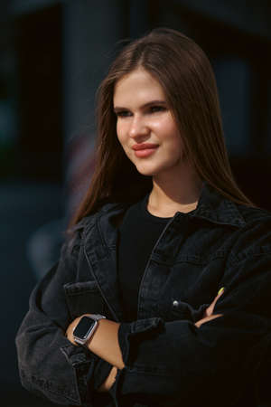 Portrait of a pretty attractive sexy young woman with natural makeup with beautiful eyes in a fashionable denim jacket in a black stylish dress. american girl walking in cityの写真素材