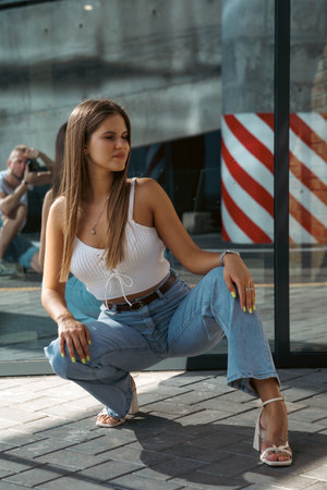 Trendy young woman in white t-shirt in vintage jeans in white shoes walks on city. Attractive girl in casual clothes is walking on the street. american style.の写真素材