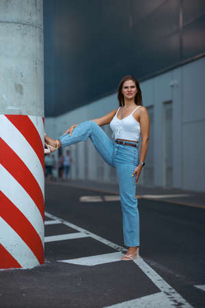 Trendy young woman in white t-shirt in vintage jeans in white shoes walks on city. Attractive girl in casual clothes is walking on the street. american style.の写真素材