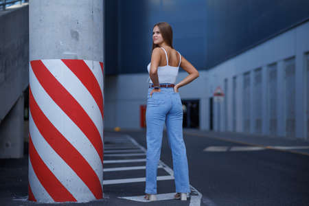 Trendy young woman in white t-shirt in vintage jeans in white shoes walks on city. Attractive girl in casual clothes is walking on the street. american style.の写真素材