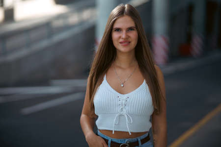Trendy young woman in white t-shirt in vintage jeans in white shoes walks on city. Attractive girl in casual clothes is walking on the street. american style.の写真素材