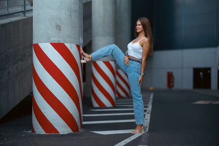 Trendy young woman in white t-shirt in vintage jeans in white shoes walks on city. Attractive girl in casual clothes is walking on the street. american style.の写真素材