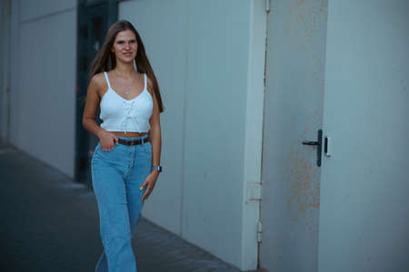 Trendy young woman in white t-shirt in vintage jeans in white shoes walks on city. Attractive girl in casual clothes is walking on the street. american style.の写真素材