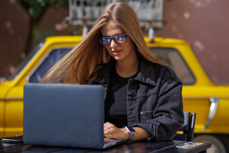 Professional young business woman in sexy glasses in black jeans jacket is working on a laptop on the Internet with a new financial project. A freelance girl works remotely in a caの写真素材
