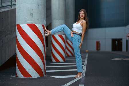 Trendy young woman in white t-shirt in vintage jeans in white shoes walks on city. Attractive girl in casual clothes is walking on the street. american style.の写真素材