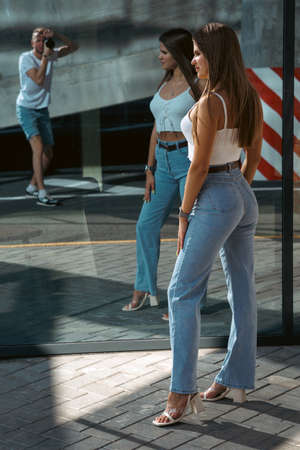 Trendy young woman in white t-shirt in vintage jeans in white shoes walks on city. Attractive girl in casual clothes is walking on the street. american style.の写真素材