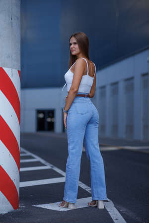 Trendy young woman in white t-shirt in vintage jeans in white shoes walks on city. Attractive girl in casual clothes is walking on the street. american style.の写真素材