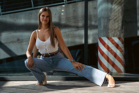 Trendy young woman in white t-shirt in vintage jeans in white shoes walks on city. Attractive girl in casual clothes is walking on the street. american style.の写真素材