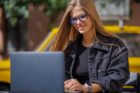 Professional young business woman in sexy glasses in black jeans jacket is working on a laptop on...