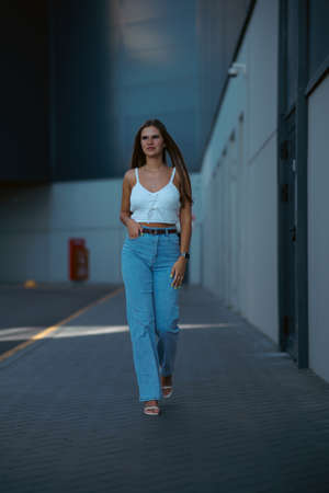 Trendy young woman in white t-shirt in vintage jeans in white shoes walks on city. Attractive girl in casual clothes is walking on the street. american style.の写真素材