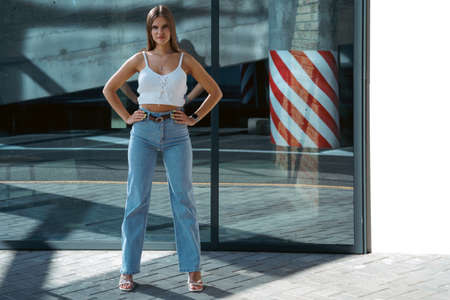 Trendy young woman in white t-shirt in vintage jeans in white shoes walks on city. Attractive girl in casual clothes is walking on the street. american style.の写真素材