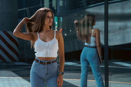 Trendy young woman in white t-shirt in vintage jeans in white shoes walks on city. Attractive girl in casual clothes is walking on the street. american style.の写真素材