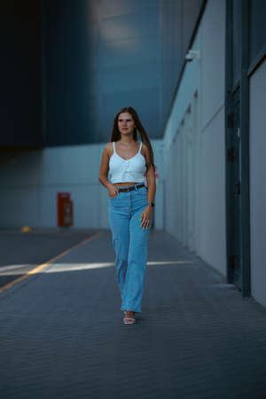Trendy young woman in white t-shirt in vintage jeans in white shoes walks on city. Attractive girl in casual clothes is walking on the street. american style.の写真素材