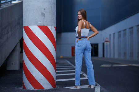 Trendy young woman in white t-shirt in vintage jeans in white shoes walks on city. Attractive girl in casual clothes is walking on the street. american style.の写真素材