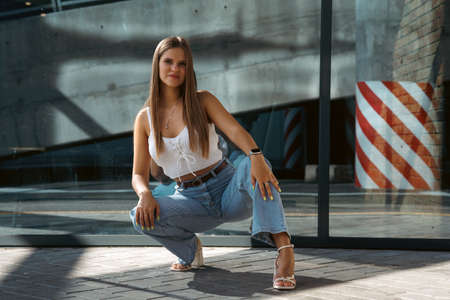 Trendy young woman in white t-shirt in vintage jeans in white shoes walks on city. Attractive girl in casual clothes is walking on the street. american style.の写真素材