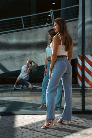Trendy young woman in white t-shirt in vintage jeans in white shoes walks on city. Attractive girl in casual clothes is walking on the street. american style.の写真素材