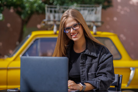 Professional young business woman in sexy glasses in black jeans jacket is working on a laptop on the Internet with a new financial project. A freelance girl works remotely in a caの写真素材