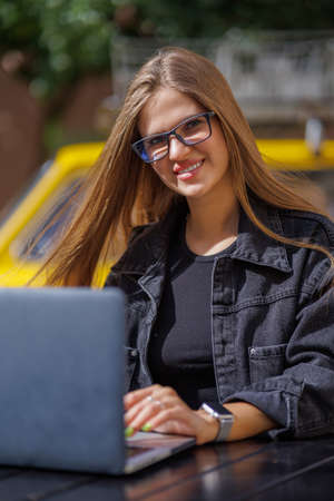 Professional young business woman in sexy glasses in black jeans jacket is working on a laptop on the Internet with a new financial project. A freelance girl works remotely in a caの写真素材