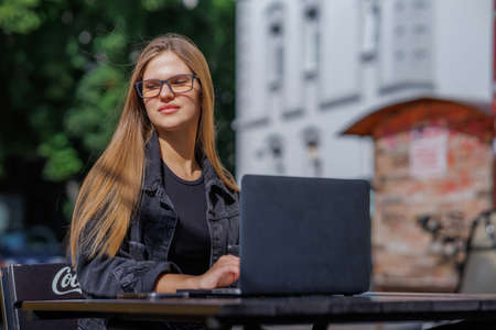 Professional young business woman in sexy glasses in black jeans jacket is working on a laptop on the Internet with a new financial project. A freelance girl works remotely in a caの写真素材