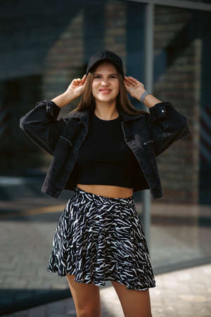 Portrait of a pretty attractive sexy young woman with natural makeup with beautiful eyes in a fashionable denim jacket in a black stylish dress. american girl walking in cityの写真素材
