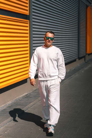 Portrait of a young guy walking around the city in a white suit and sunglasses