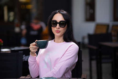 Portrait pretty trendy young brunette woman in stylish clothing with vintage cup in cafe. Elegant cute girl fashion model enjoys coffee break indoors. Morning for caffeine lovers.の写真素材