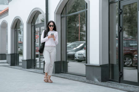 Gorgeous young woman in fashion clothes walk at the street. Attractive girl model in casual outfit walk on city street near vintage building. side view.の写真素材