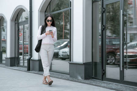 Gorgeous young woman in fashion clothes walk at the street. Attractive girl model in casual outfit walk on city street near vintage building. side view.の写真素材