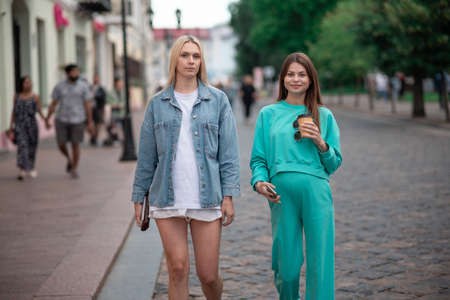 Two cool fashionable pregnant girlfriends in fashionable clothes are walking down the street and talking. Friends share secrets and discuss the birth of children.の写真素材