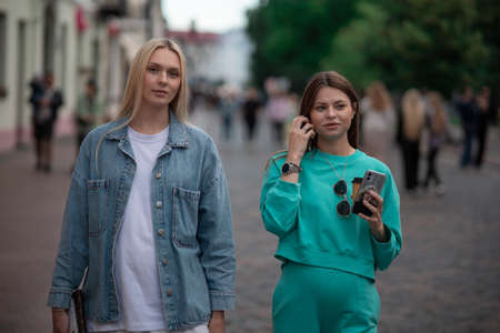 Two cool fashionable pregnant girlfriends in fashionable clothes are walking down the street and talking. Friends share secrets and discuss the birth of children.の写真素材