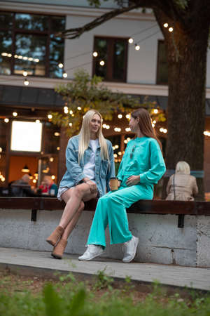 Positive pregnant girls in fashionable clothes talk and have a good time. Attractive happy girls socialize outdoors. Preparation for the birth of a child.の写真素材