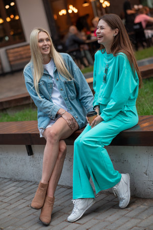 Positive pregnant girls in fashionable clothes talk and have a good time. Attractive happy girls socialize outdoors. Preparation for the birth of a child.の写真素材